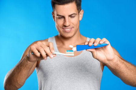 Man applying toothpaste on brush against blue backgroundの写真素材