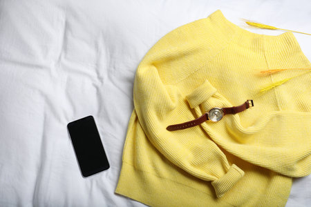 Yellow warm sweater with smartphone and wristwatch on bedsheet, flat layの写真素材