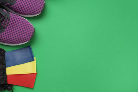 Fitness elastic bands and training shoes on green background, flat lay. Space or textの写真素材