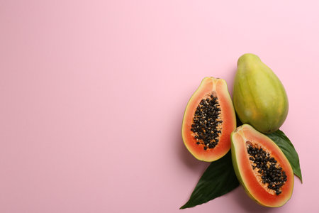 Fresh ripe papaya fruits with green leaves on pink background, flat lay. Space for textの写真素材