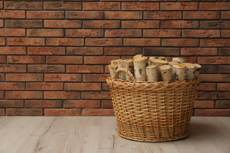 Wicker basket with firewood near brick wall indoors, space for textの写真素材