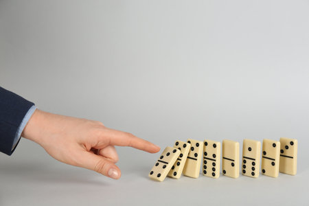 Woman causing chain reaction by pushing domino tile on gray background, closeup. Space for textの写真素材