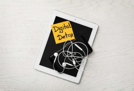 Different gadgets and sticking paper with words DIGITAL DETOX on white wooden background, top viewの写真素材