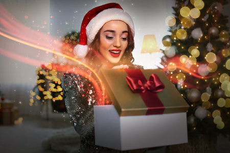 Beautiful woman in Santa hat opening Christmas gift at homeの写真素材
