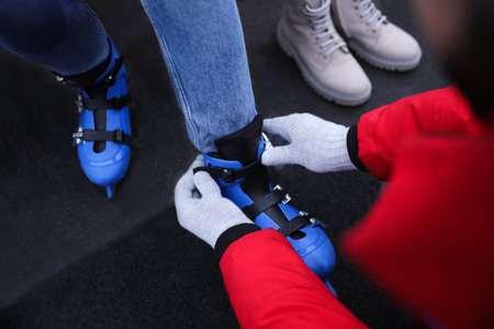 Young man helping his girlfriend to put on ice skates outdoors, above view