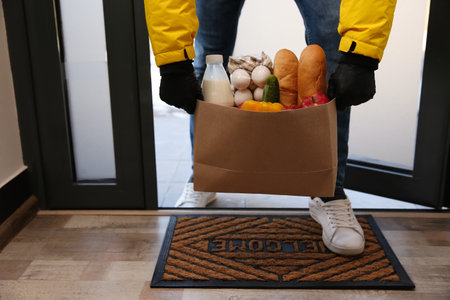 Courier bring paper bag with food to doorway, closeup. Delivery service during quarantine due to Covid-19 outbreakの写真素材