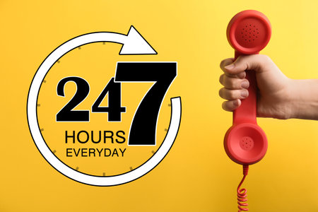 24/7 hotline service. Woman holding handset on yellow background, closeupの写真素材