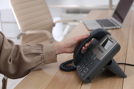 Woman using desktop telephone at wooden table in office, closeup. hotline serviceの写真素材