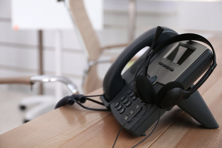 Desktop telephone and headset on wooden table in office, space for text. hotline serviceの写真素材