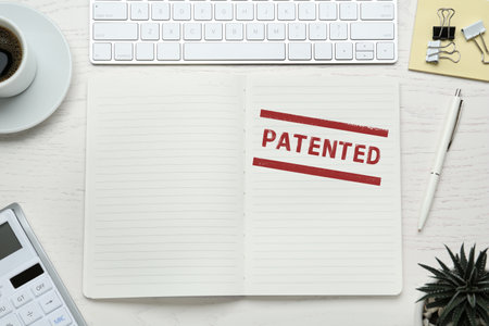 Notebook with stamp PATENTED and computer keyboard on white wooden table,flat layの写真素材