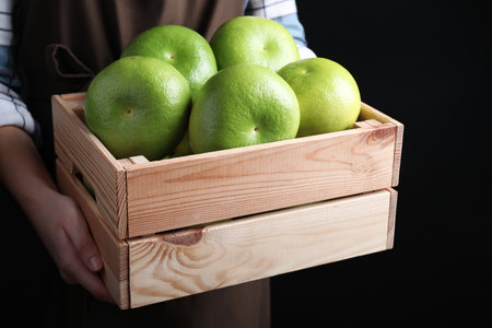 Woman holding wooden crate with sweetie fruits on black background, closeupの写真素材