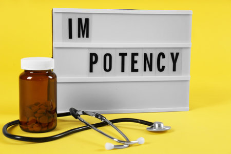 Lightbox with word IMPOTENCY, jar of pills and stethoscope on yellow backgroundの写真素材