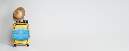 COVID-19 pandemic, travel during coronavirus outbreak. Suitcase with protective mask on light background, space for textの写真素材