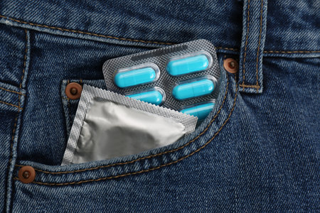 Jeans with pills and condom in pocket as background, top view. Potency problem conceptの写真素材