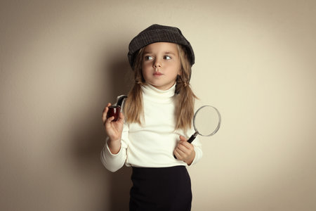 Cute little child in hat with smoking pipe and magnifying glass playing detective on beige backgroundの写真素材