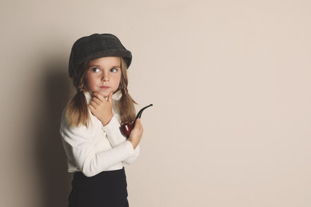 Cute little child in hat with smoking pipe playing detective on beige background, space for textの写真素材
