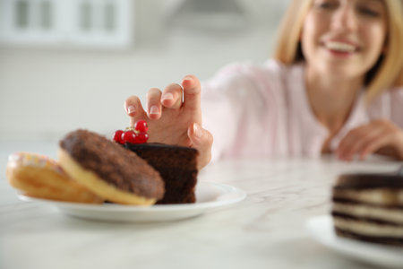 Concept of choice between healthy and junk food. Woman with sweets at white table in kitchen, focus on handの写真素材