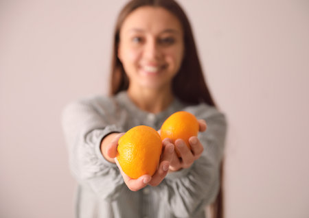 Woman with fresh tangerines on beige background, focus on fruitsの写真素材