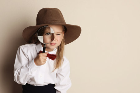 Cute little child in hat with magnifying glass playing detective on beige background, space for textの写真素材