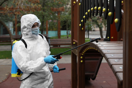 Woman wearing chemical protective suit with disinfectant sprayer on playground.の写真素材