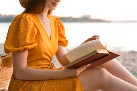 Young woman reading book on sandy beach near sea, closeupの写真素材