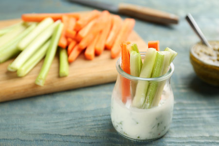 Celery and other vegetable sticks with dip sauce in glass jar on light blue wooden table. Space for textの写真素材