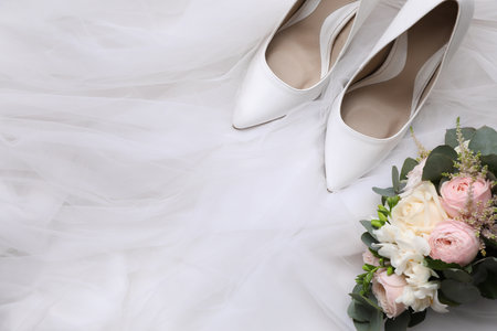Pair of wedding high heel shoes and beautiful bouquet on white veil, flat lay. Space for textの写真素材