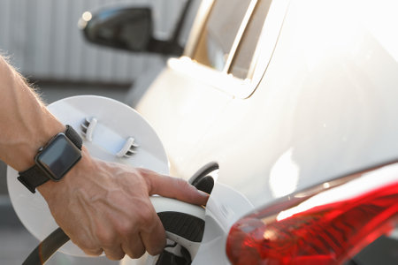 Man inserting plug into electric car socket at charging station, closeup
