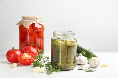 Glass jars of pickled cucumbers and tomatoes on white tableの写真素材