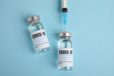 Filling syringe with coronavirus vaccine on light blue background, flat lay