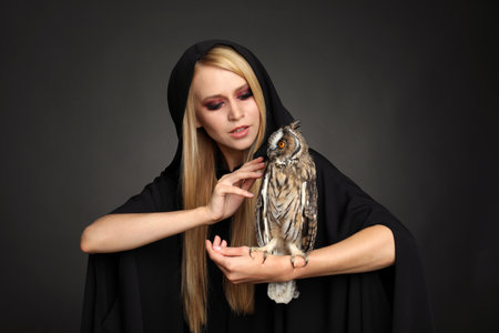 Witch in black mantle with owl on dark background. Scary fantasy characterの写真素材