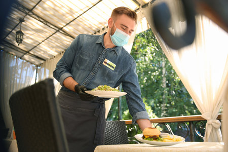 Waiter serving food in restaurant. Catering during coronavirus quarantineの写真素材