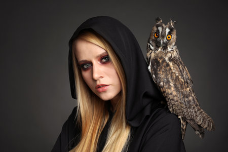 Witch in black mantle with owl on dark background. Scary fantasy characterの写真素材