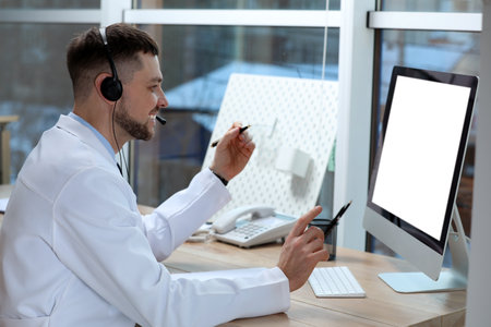 Doctor with headset consulting patient online at desk in clinic, space for text. Health service hotlineの写真素材
