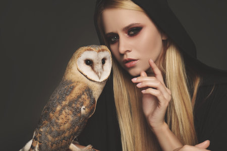 Witch in black mantle with owl on dark background. Scary fantasy characterの写真素材