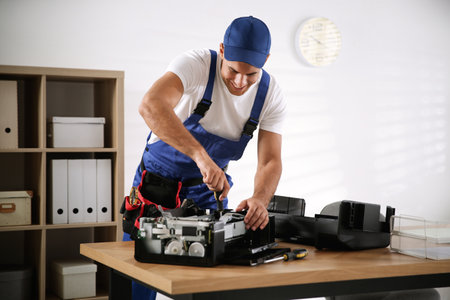 Repairman with screwdriver fixing modern printer in officeの写真素材