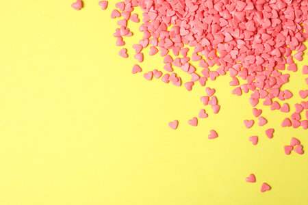 Bright heart shaped sprinkles on yellow background, flat lay. Space for text