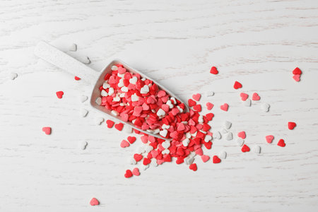 Bright heart shaped sprinkles and scoop on white wooden table, flat layの写真素材
