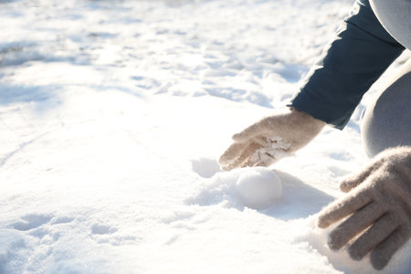 Woman rolling snowball outdoors on winter day, closeup. Space for textの写真素材