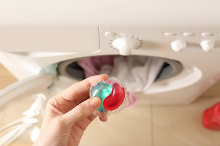 Woman holding laundry detergent capsule near washing machine indoors, top viewの写真素材