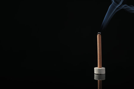 Incense stick smoldering in holder on black background. Space for textの写真素材