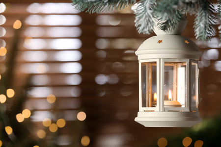 Beautiful Christmas lantern with burning candle hanging on fir tree branch in room. Space for textの写真素材