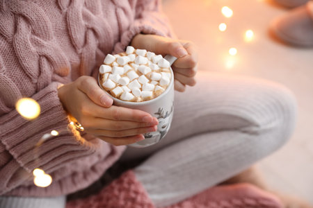 Woman holding cup of hot drink with marshmallows indoors, closeup. Magic Christmas atmosphereの写真素材