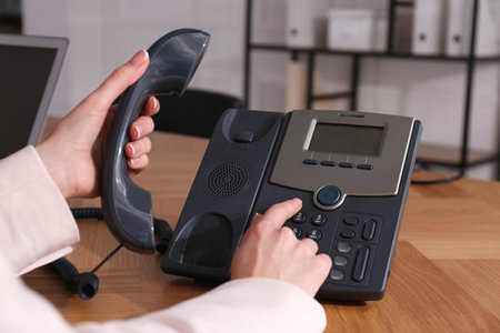 Woman using desktop telephone at wooden table in office, closeup. hotline serviceの写真素材