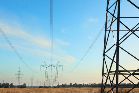 High voltage towers with electricity transmission power lines in the field on sunny day
