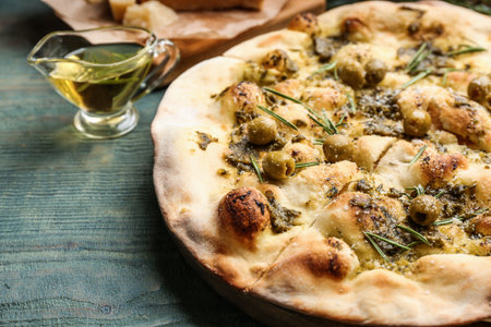 Traditional Italian focaccia bread with pesto, olives and rosemary on blue wooden table, closeup