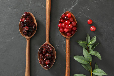 Flat lay composition with dried and fresh cranberries in wooden spoons on dark tableの写真素材