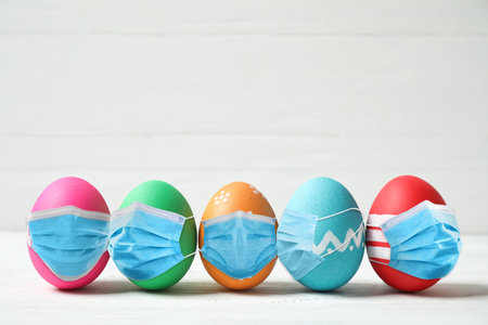 Colorful Easter eggs in protective masks on white wooden backgroundの写真素材
