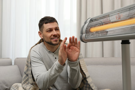 Man warming hands near electric infrared heater at homeの写真素材