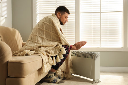 Man warming hands near electric heater at home